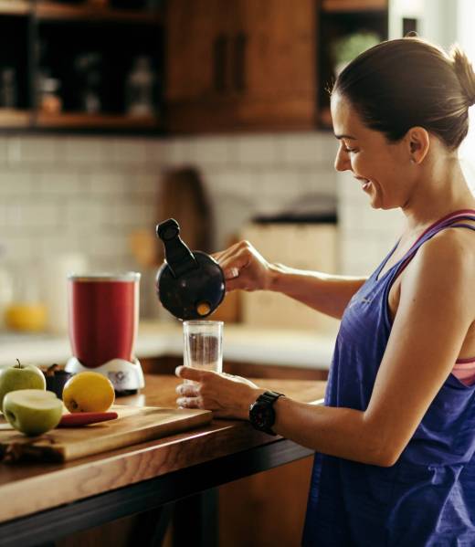 Happy athletic woman pouring fruit smoothie in a glass in the kitchen.